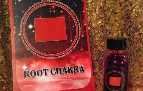 A bottle of root chakra oil sitting next to a book.